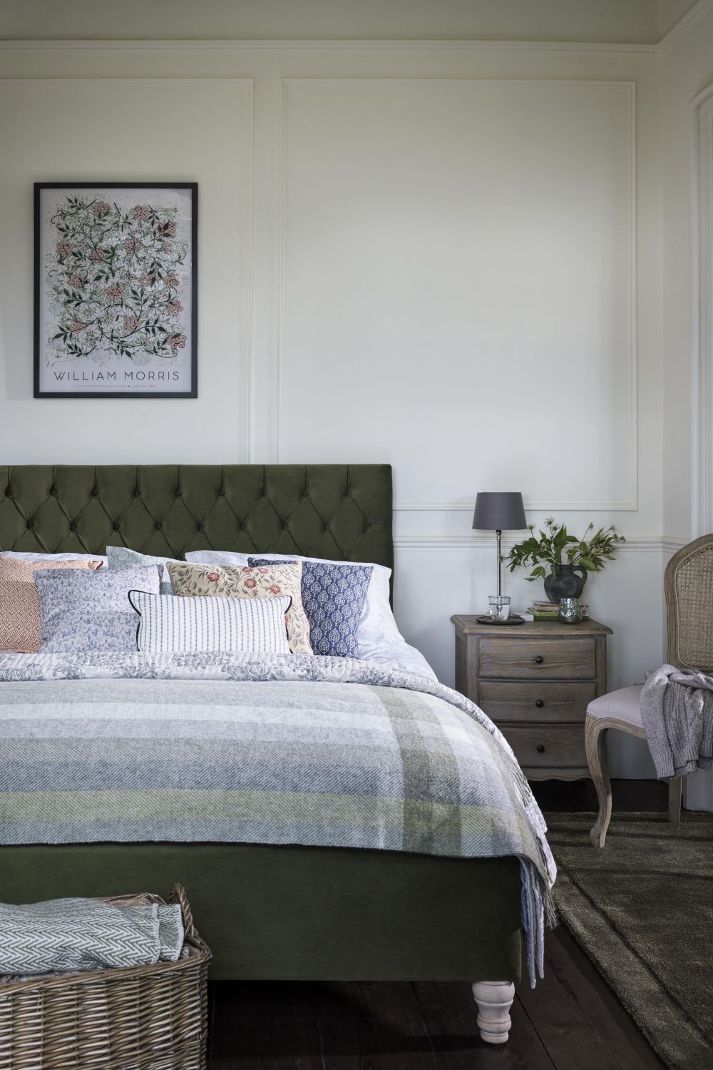 Make your guest bedroom welcoming with a neatly made bed featuring a green headboard, patterned bedding, and decorative pillows. The room is enhanced by a framed William Morris print hanging above, sure to make