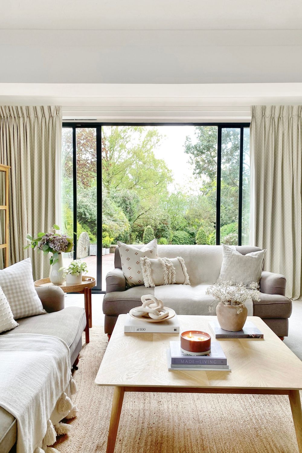 A cozy living room with a sofa, armchairs, and a wooden coffee table, overlooking a garden through large windows featuring advanced door and window design for enhanced security.