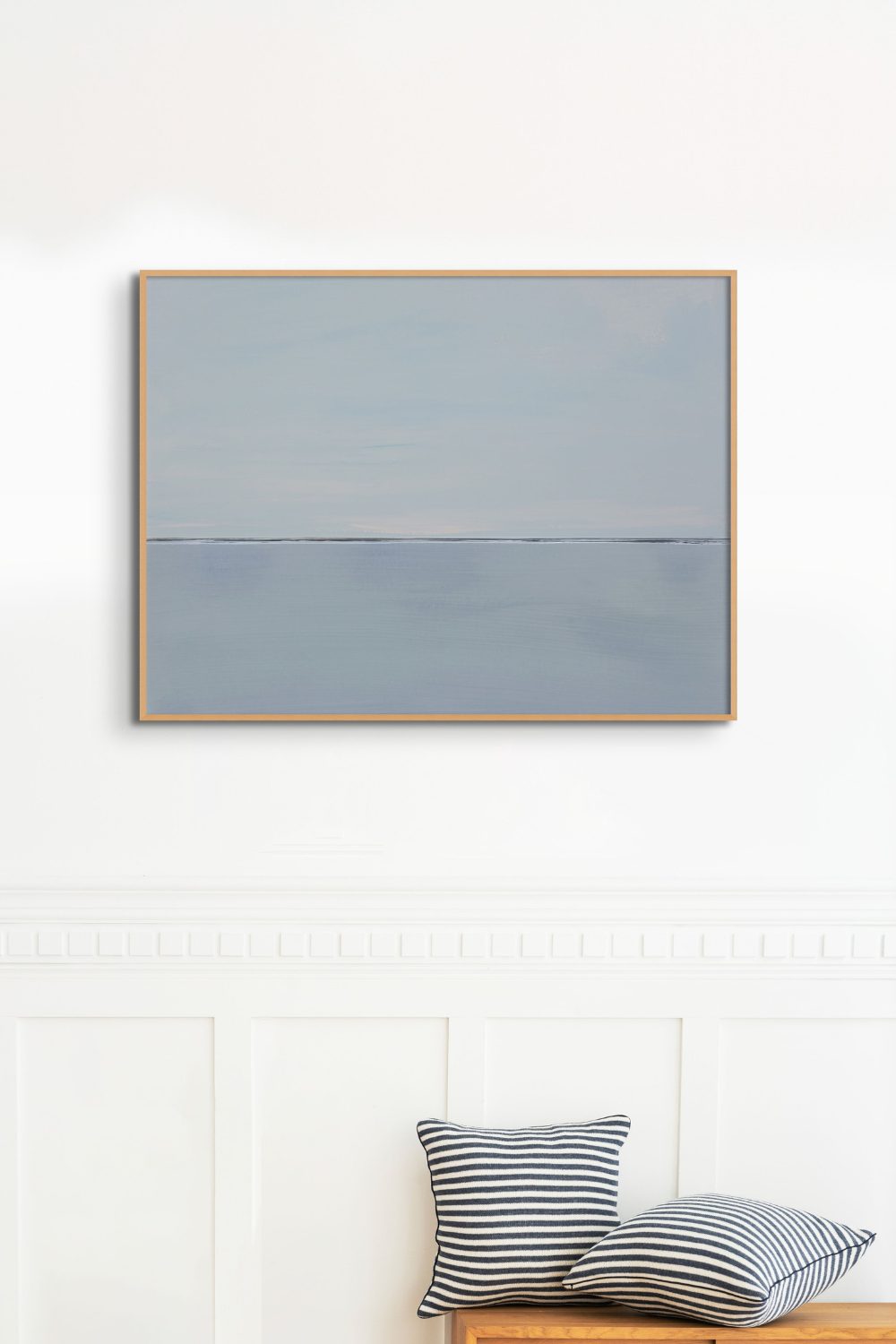 Minimalist slate-grey sea painting above a wooden seat with black and white striped cushions