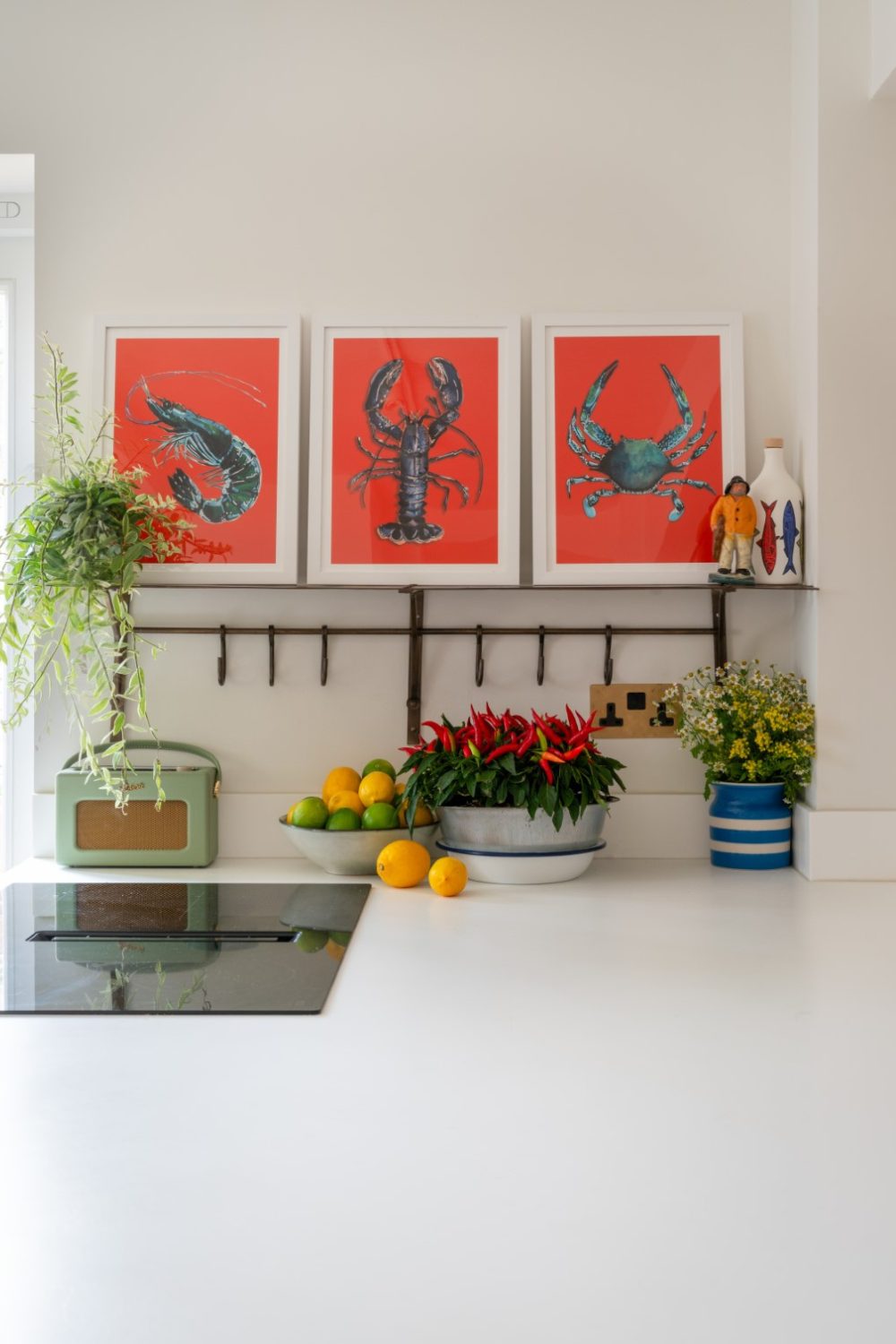 Three bright red crustacean paintings in a white kitchen with plants