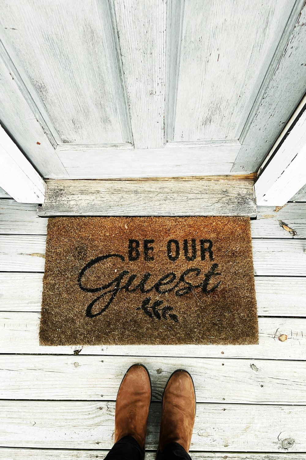 Brown welcome mat in front of white distressed wood front door