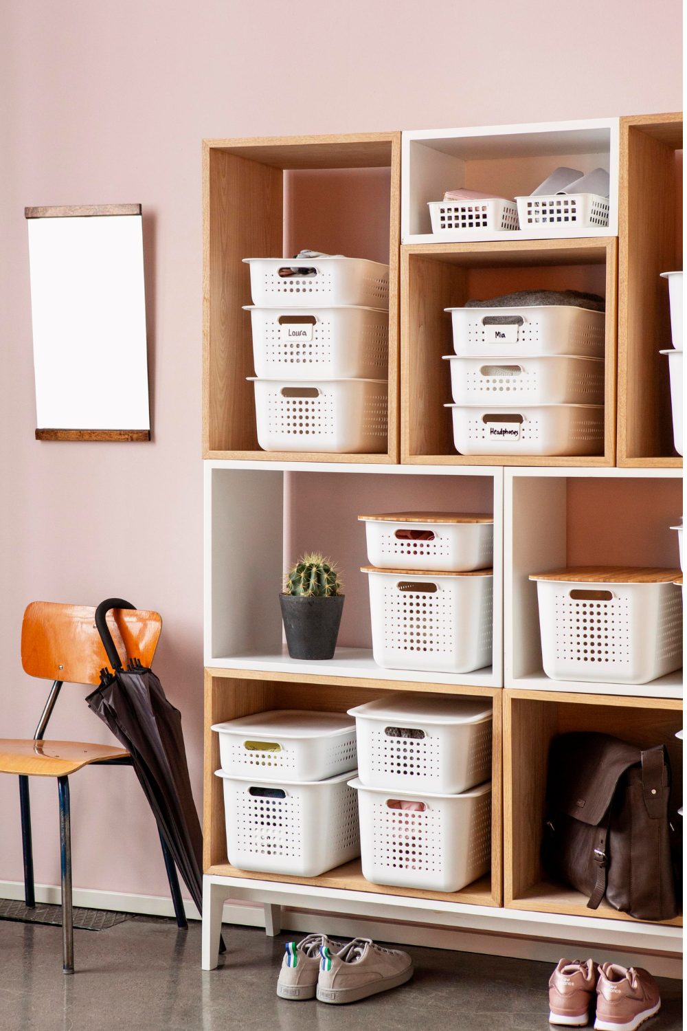 Shelving unit with white baskets against a pink wall, with shoes and umbrella