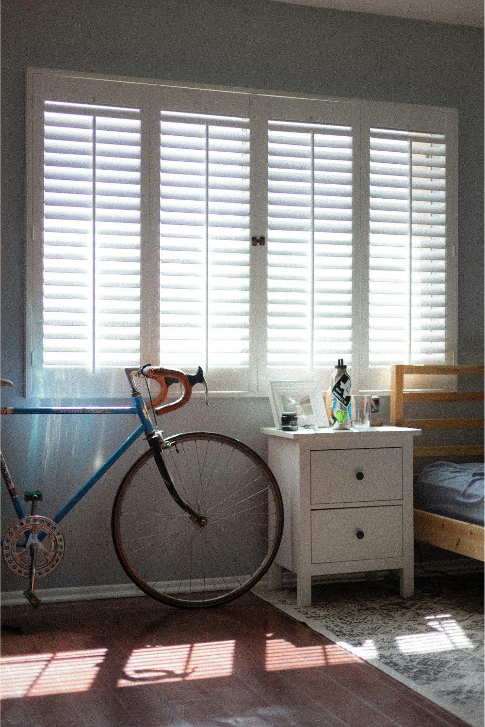 A shaded bedroom with window shutters and bicycle