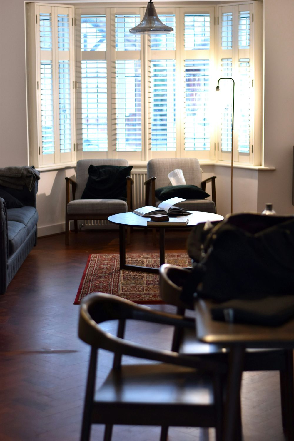 Living room with dark floor, red rug and bay window shutters