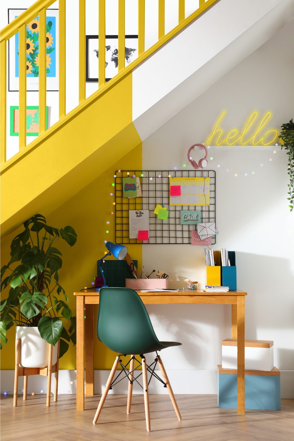 Wooden desk under bright yellow and white staircase with neon sign and colourful noticeboard