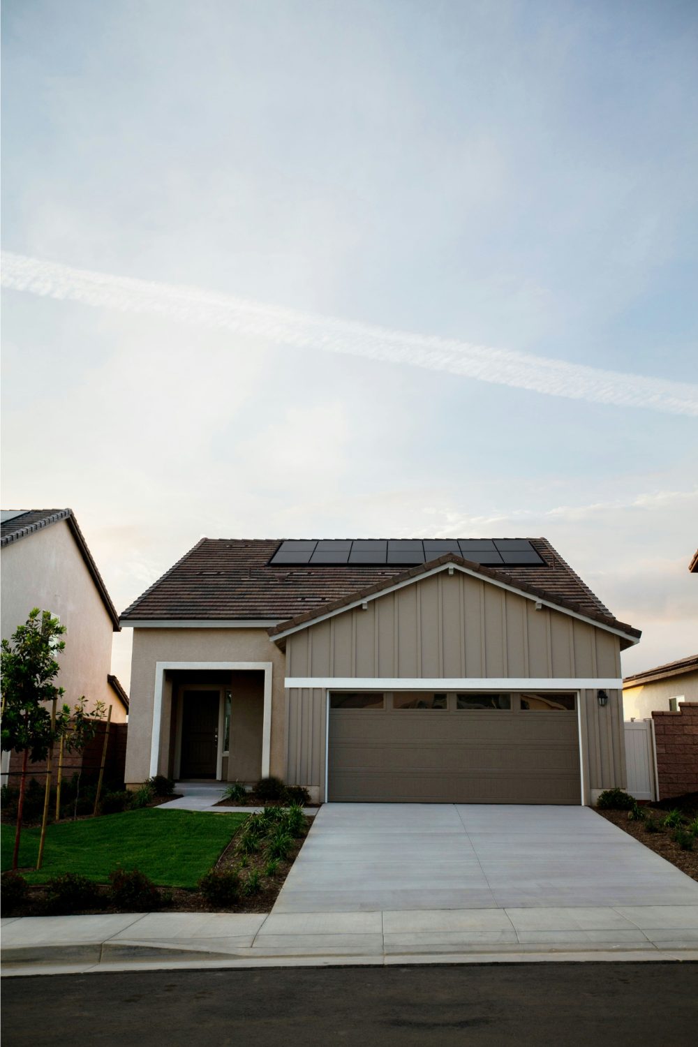 Grey garage and house with expanse of blue sky above it.