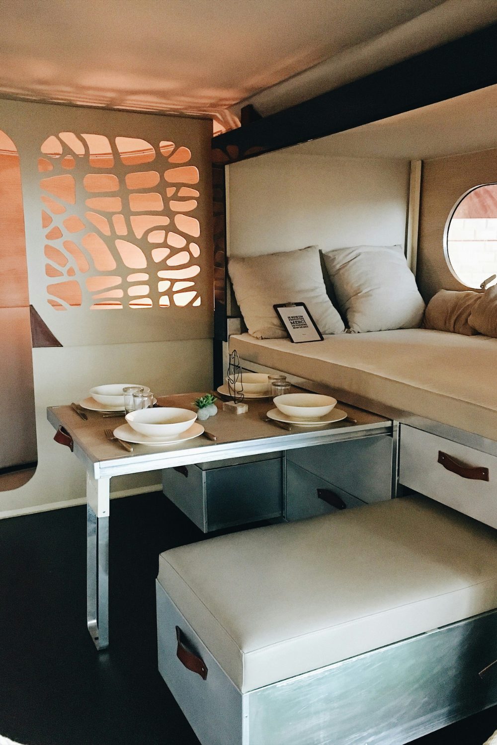 White and neutral minimalist van interior with bed, pull-out table and seats, and decorative screen