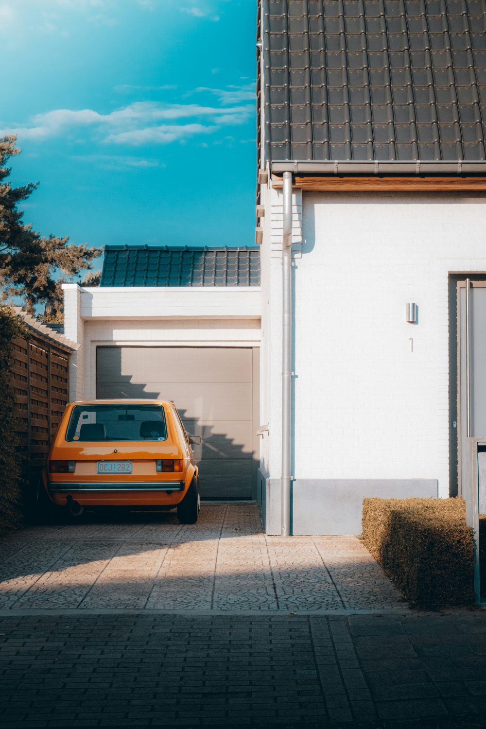 Vibrant blue sky above a white house and garage with orange car parked in front