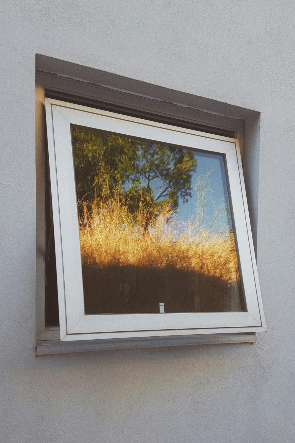 An open window in a grey wall with the reflection of a vibrant natural landscape