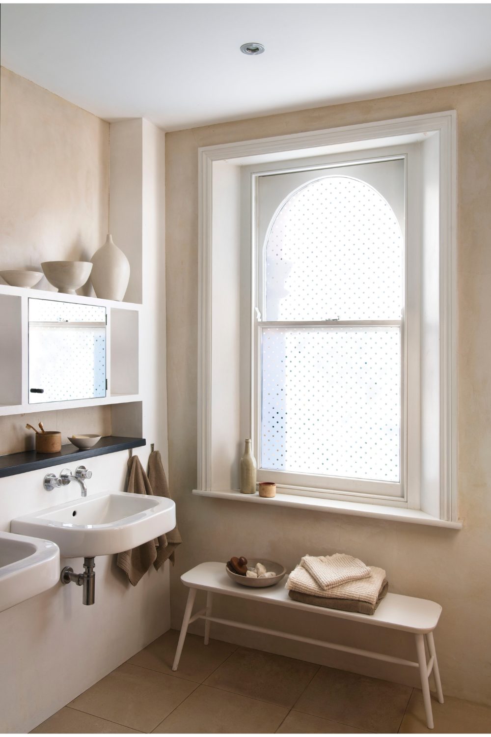 Neutral bathroom with wooden bench below large window with polka dot design