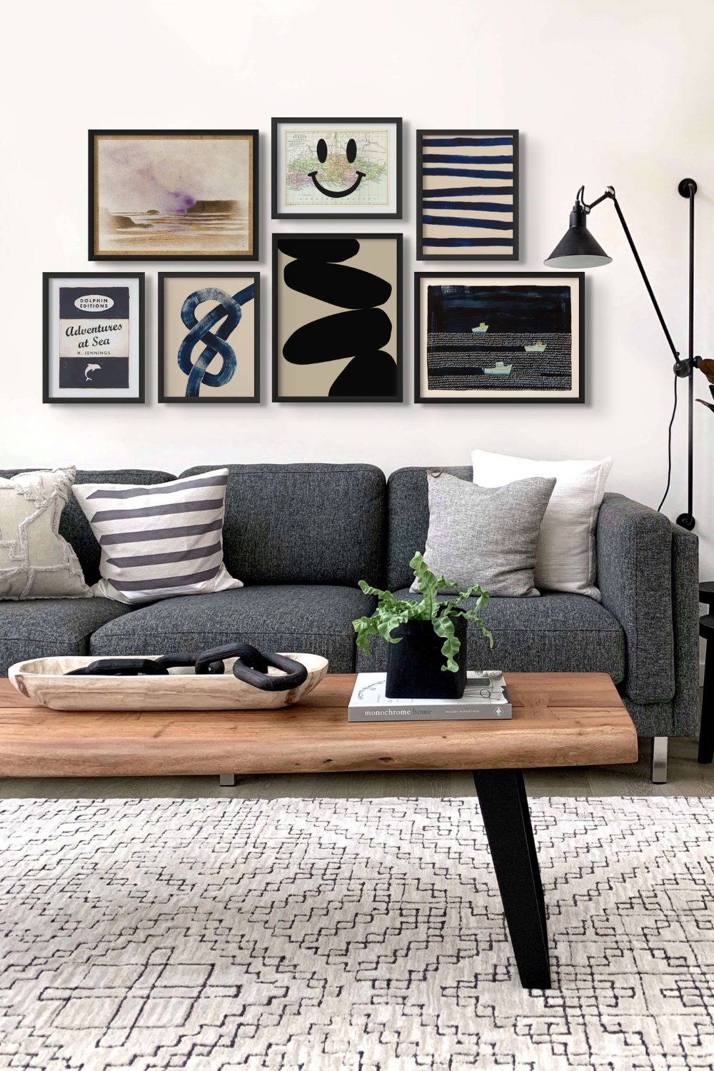 Selection of black and white prints above grey sofa with cushions, wooden coffee table and white rug