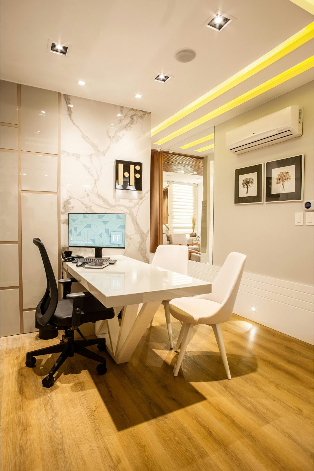 White desk and chairs on wooden floor next to white marble wall with yellow light feature