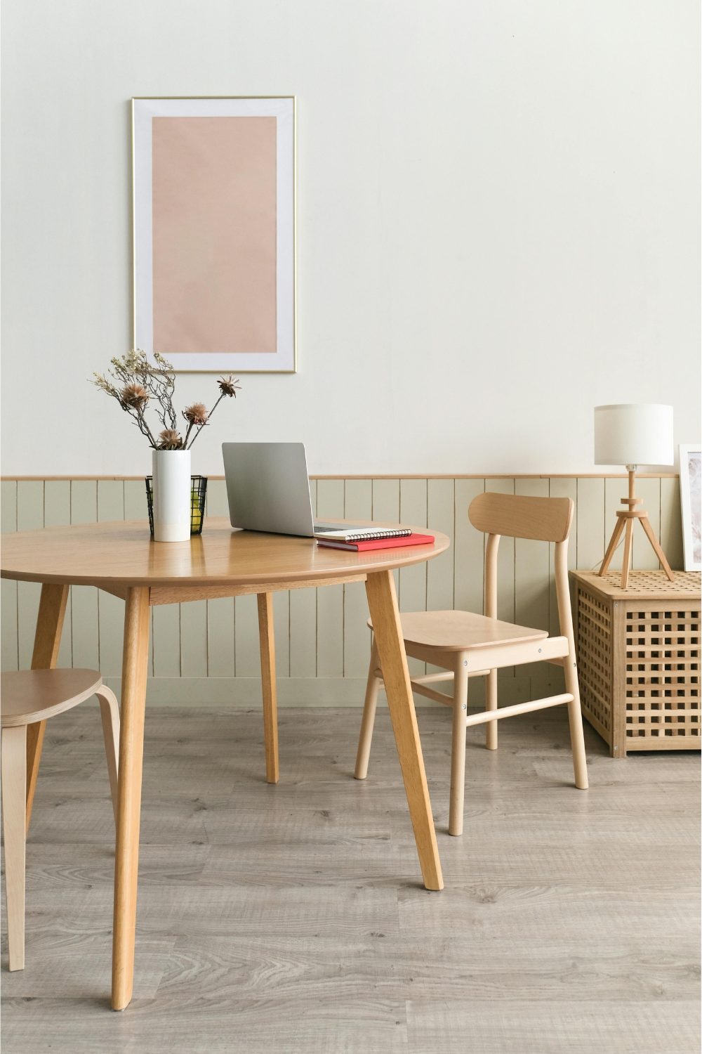 Light wooden desk and chairs with laptop, plant pot and lamp against a muted green wall