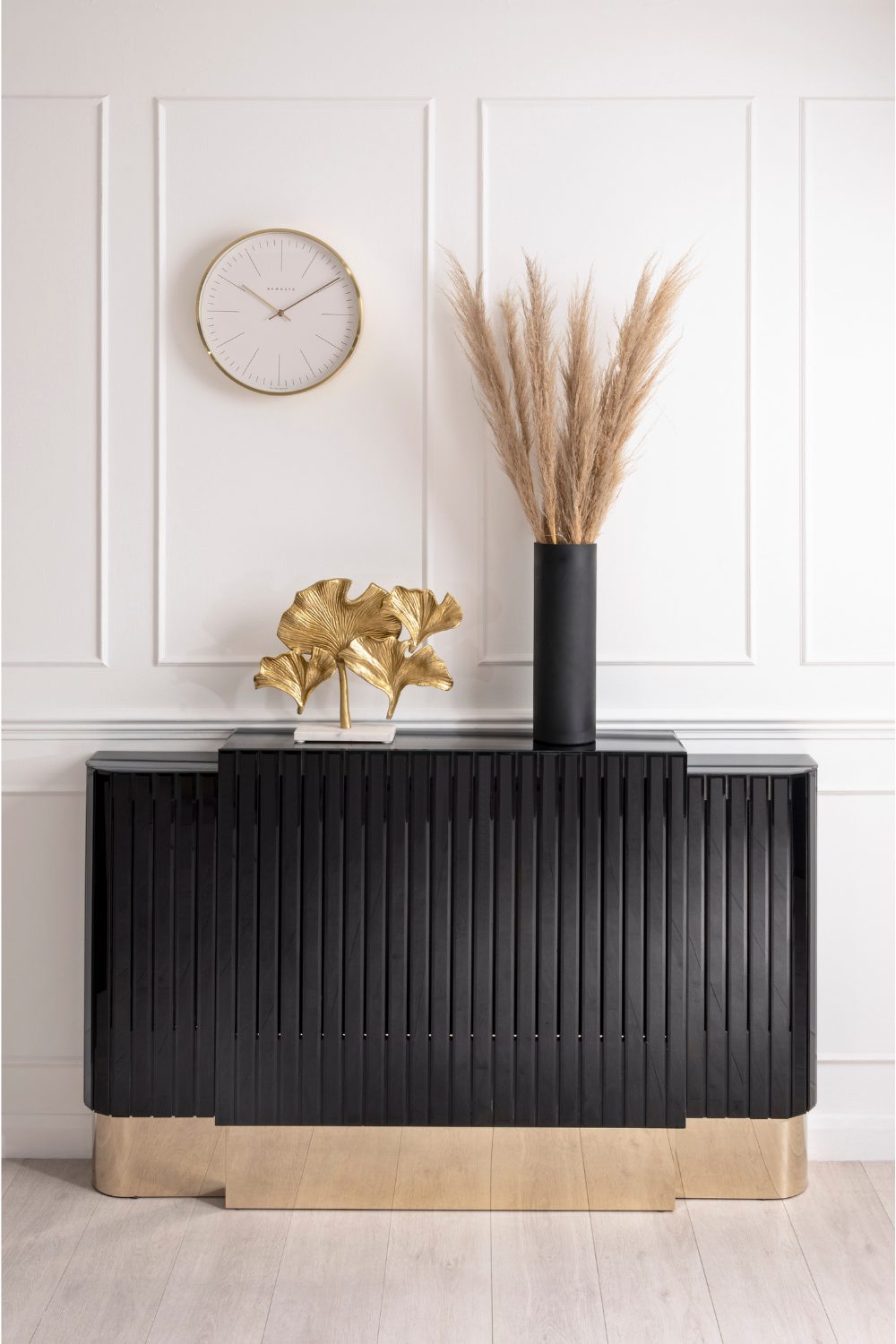 Black and gold radiator with a gold leaf sculpture and a black vase against a white panelled wall