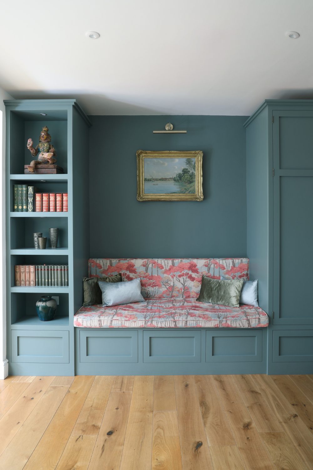 Dusky blue loveseat and cabinet with tree-patterned cushion and gold-framed landscape painting