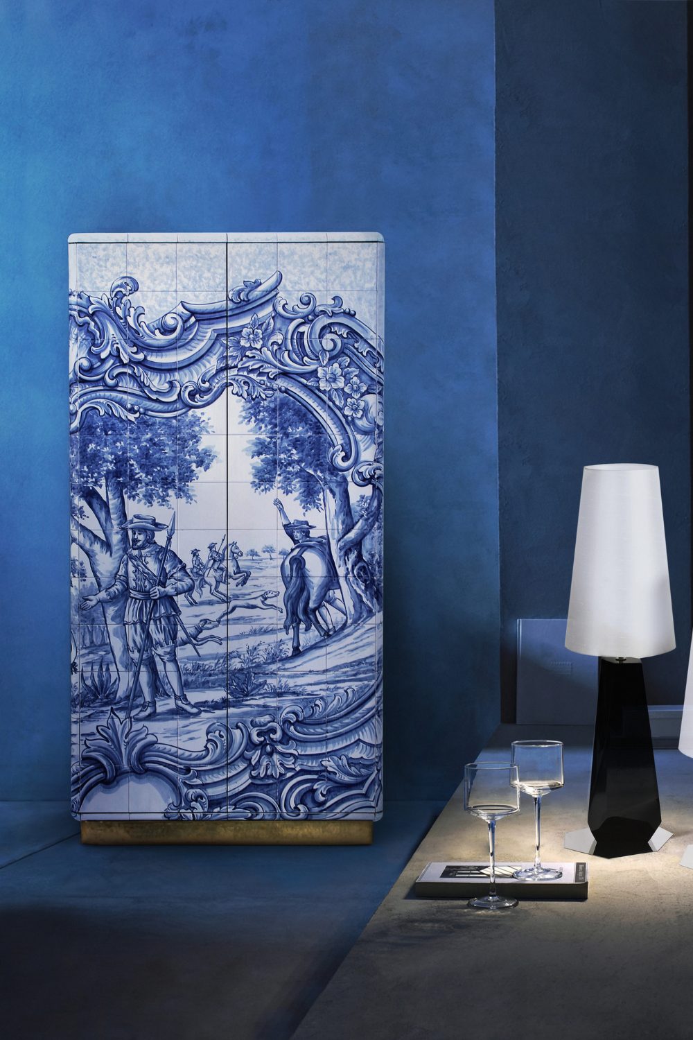 Wardrobe with blue and white porcelain tile design against a dark blue wall next to table with lamp and glasses