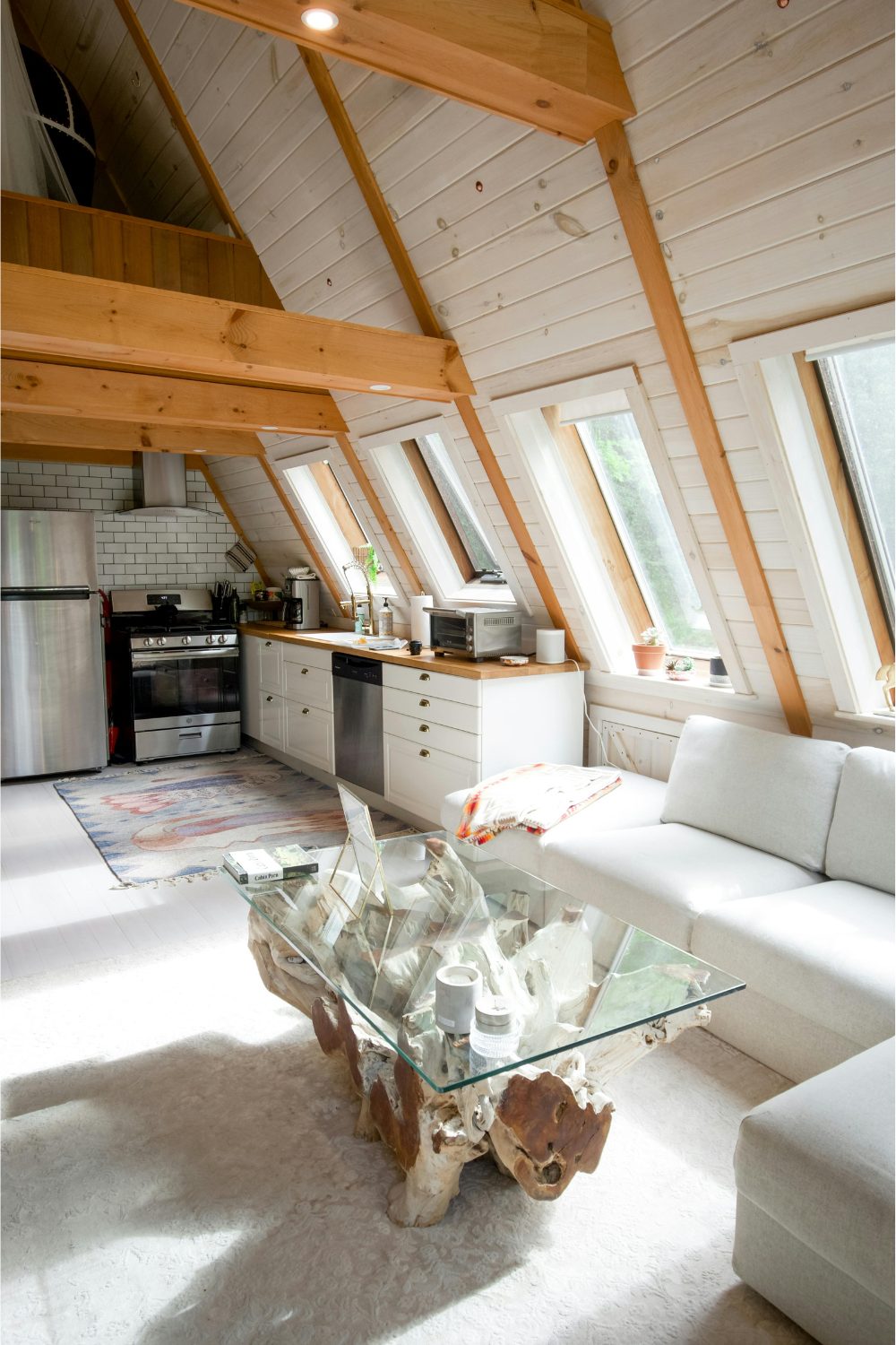 White kitchen on the upper floor of a barn conversion with a glass and wood coffee table next to a white sofa