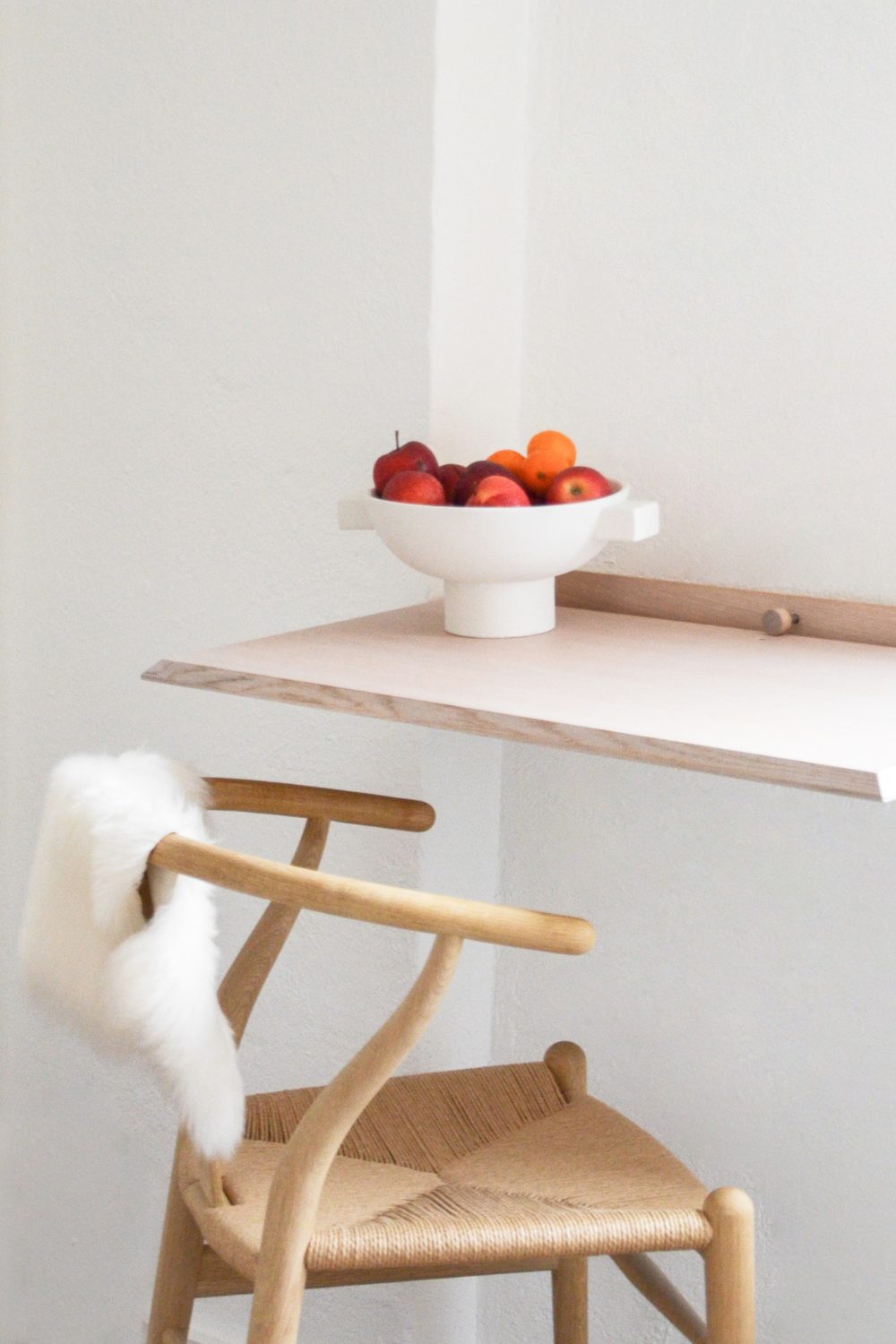 Wooden folding desk with white bowl of red apples next to wooden chair