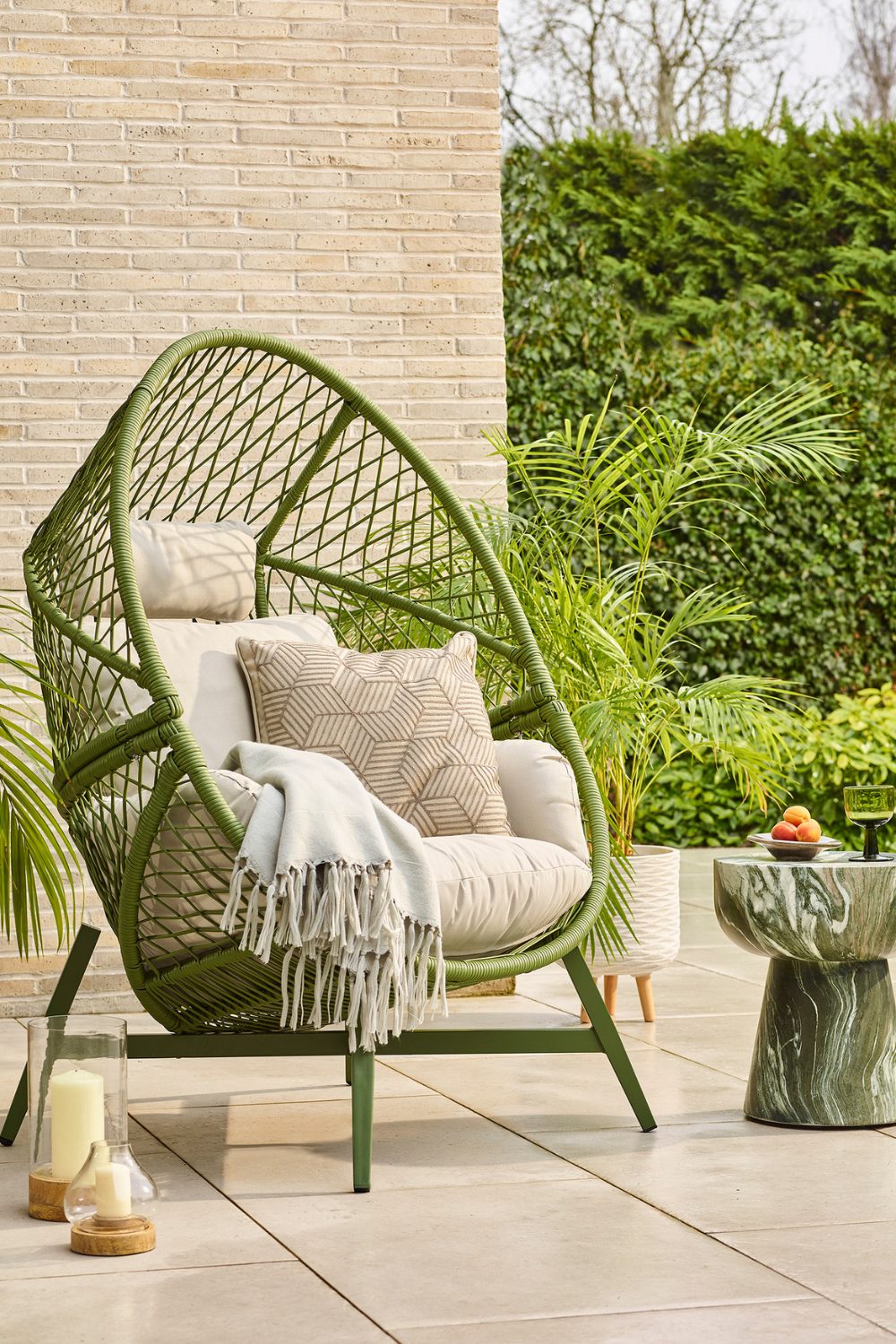 Green wire chair with white cushions in garden with white paving