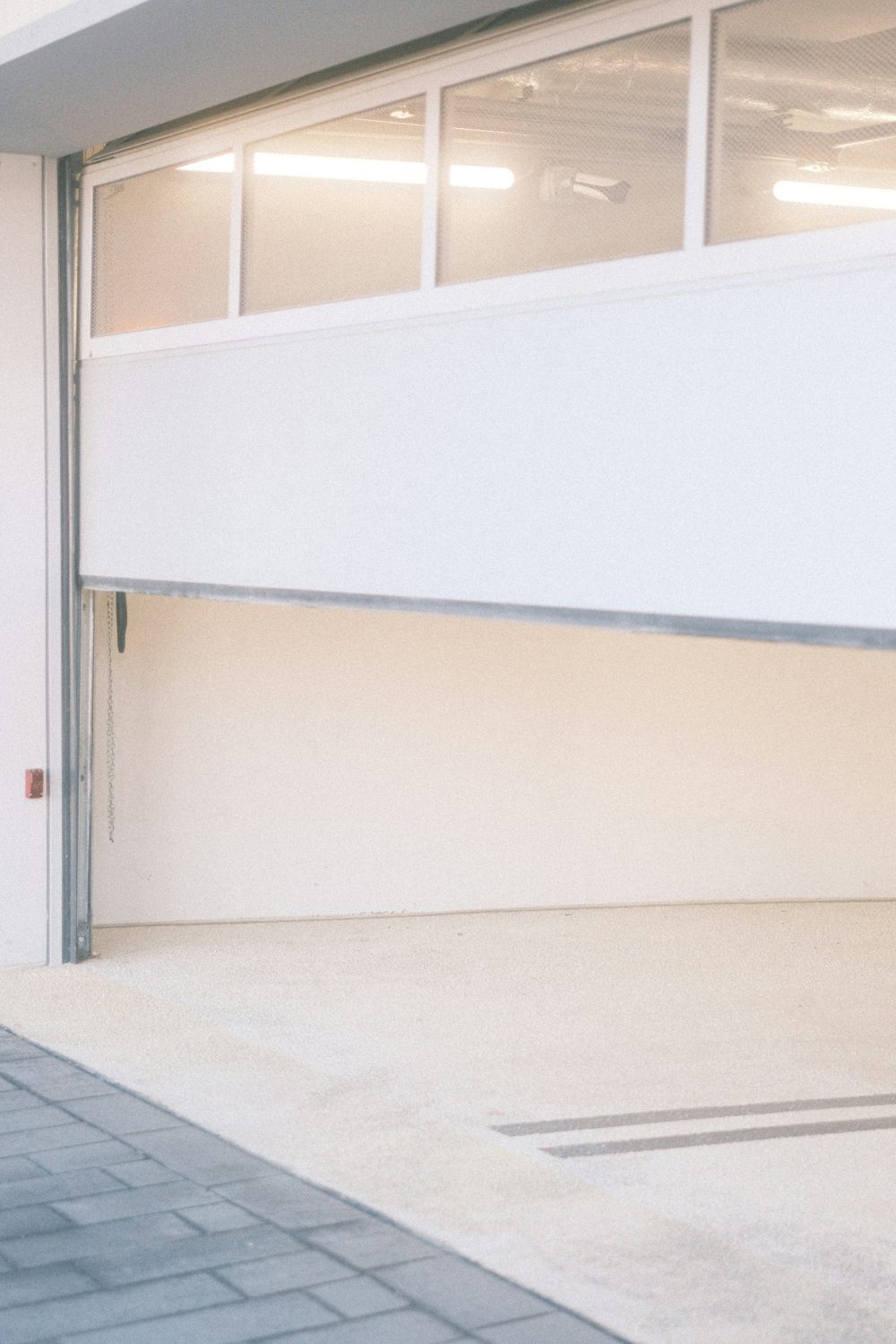 Driveway of a a garage with half open glass door showing white interior