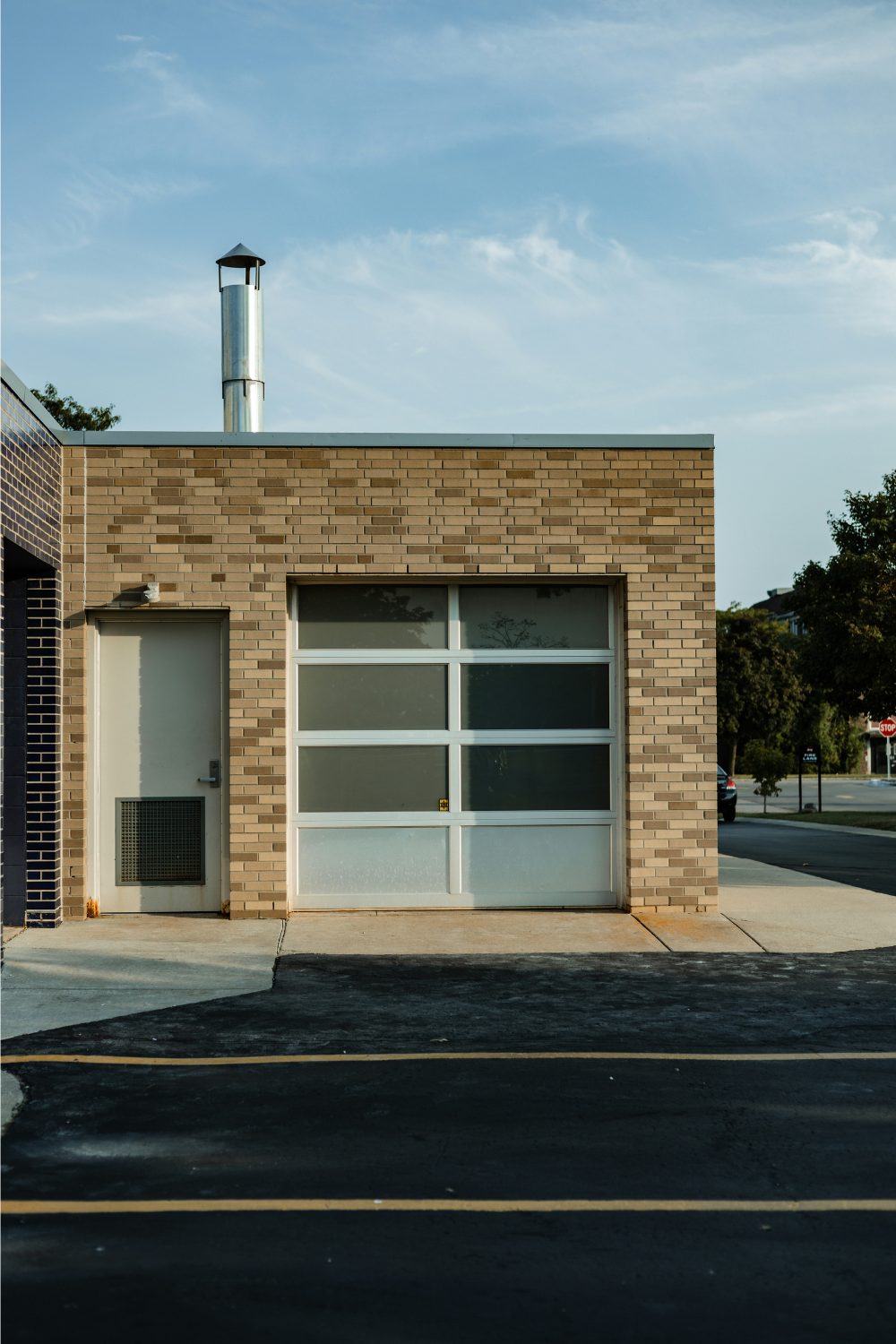 Exterior of a brick garage with panelled glass door against a blue sky with tarmac road in foreground