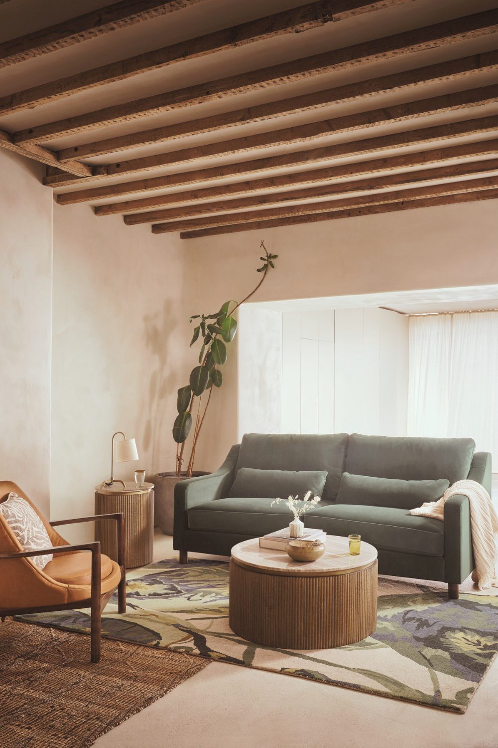 Green sofa in neutral living room with wooden coffee table, timbered ceiling, and leaf patterned rug