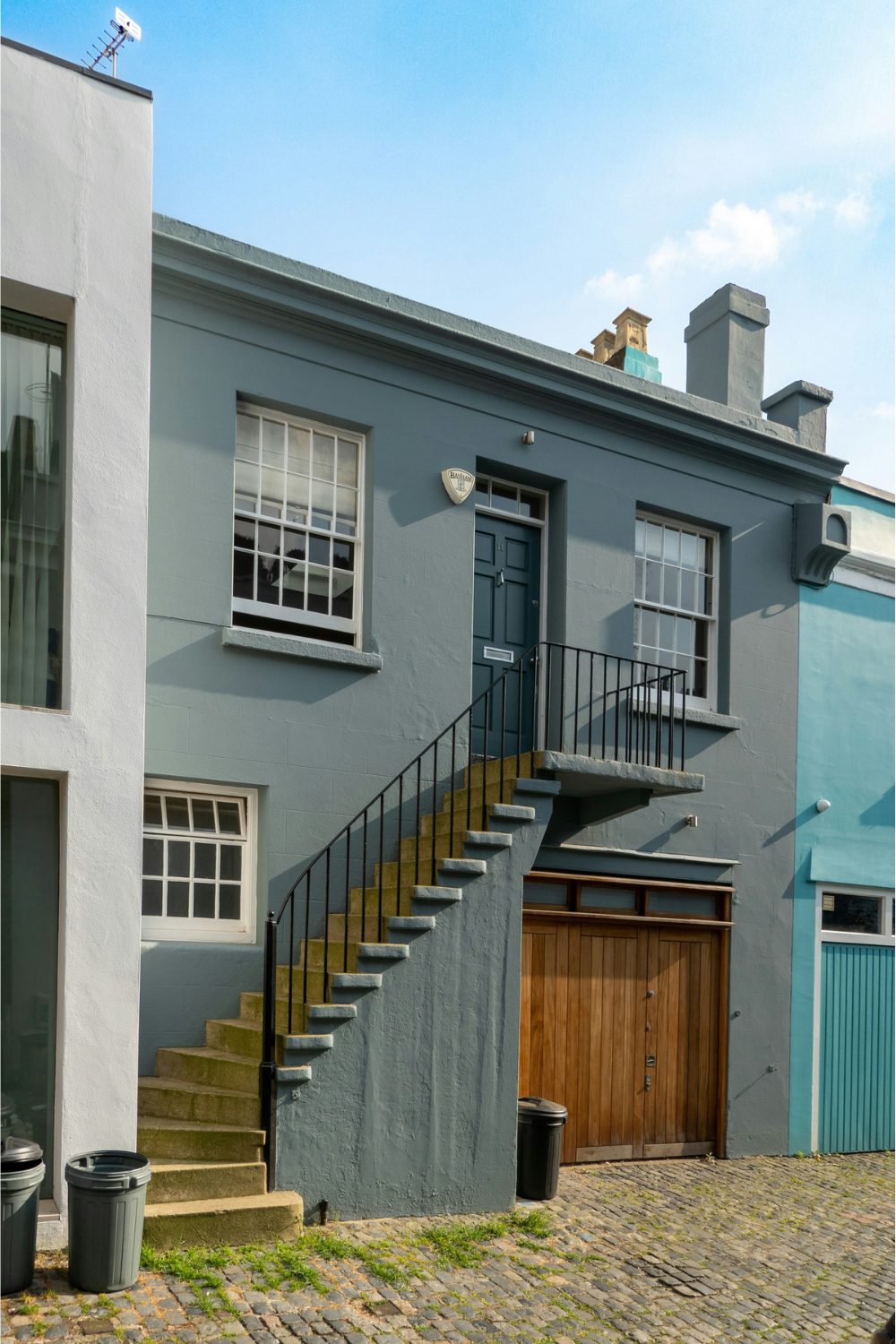 Grey house on cobbled street with wooden garage door below long stairs leading to black front door