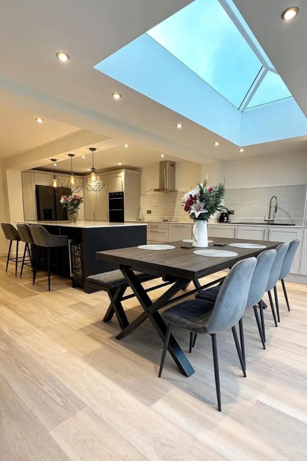 Modern kitchen with spotlights, dark wood table and grey chairs under a large skylight