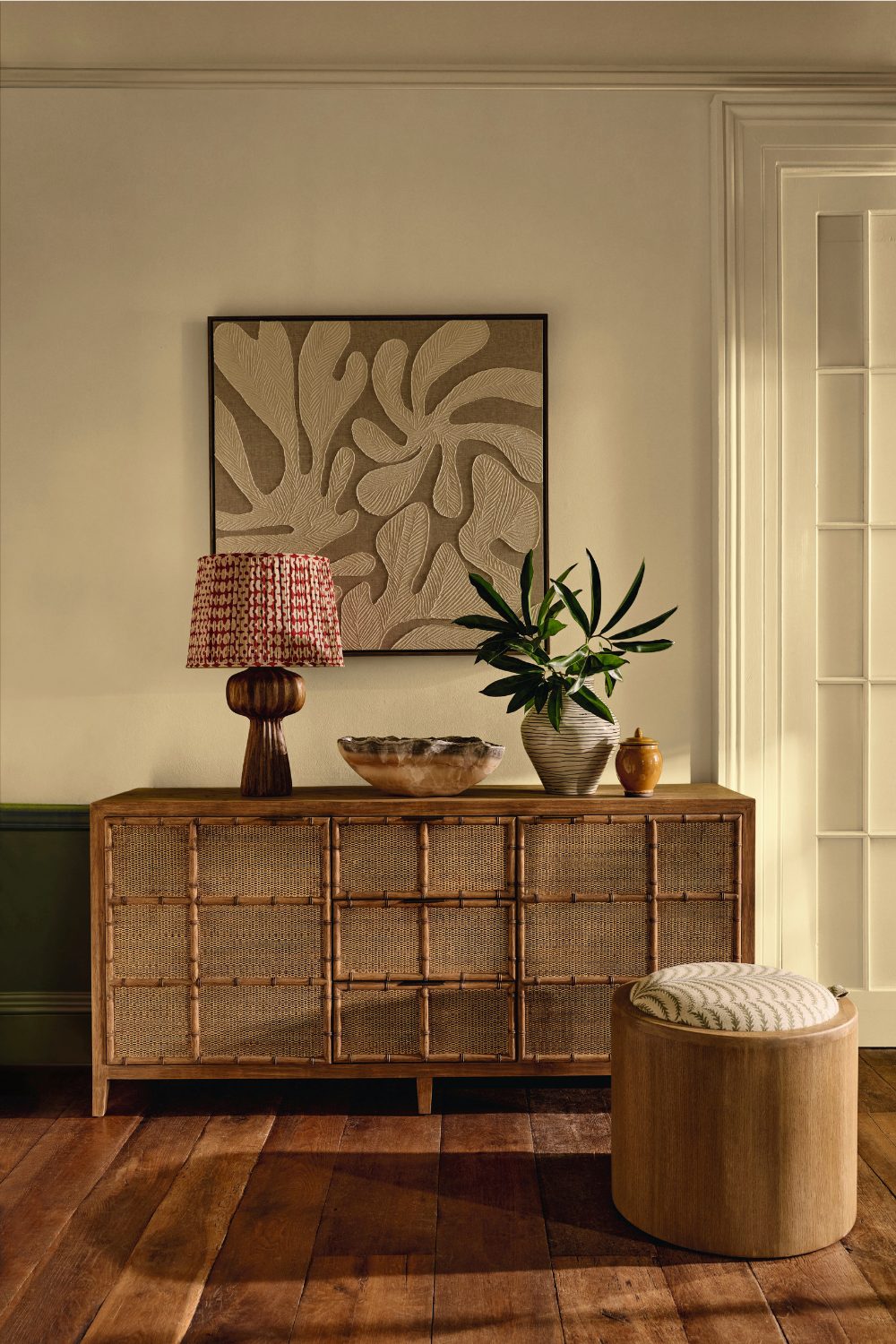 Bamboo sideboard with lamp and vase below brown framed print on a wooden floor