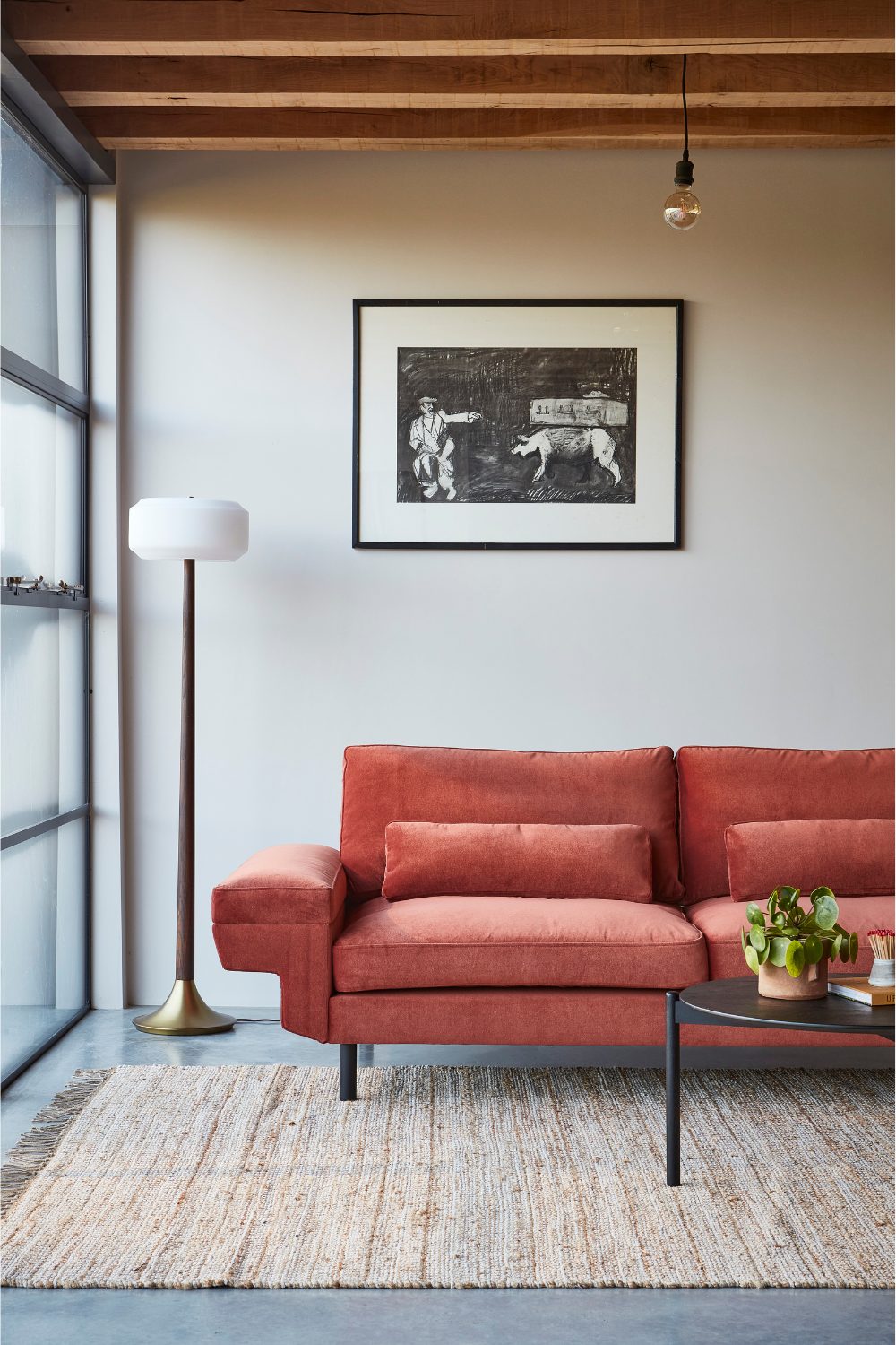 Red sofa behind black coffee table under framed print and lamp
