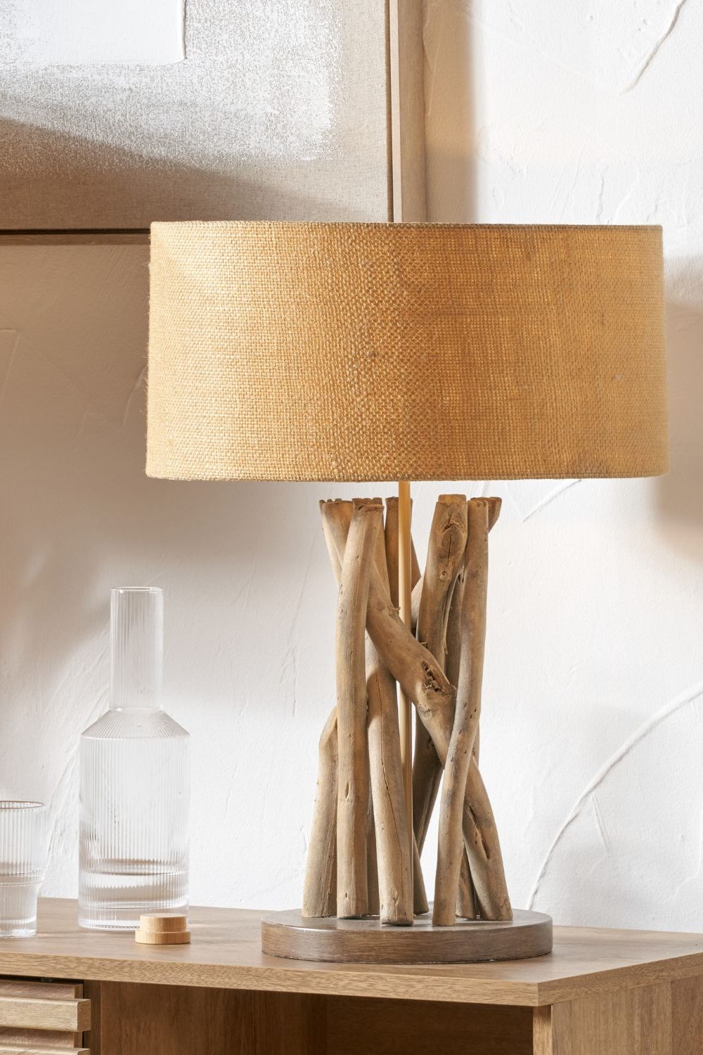 Rough woven lampshade with driftwood base on a wooden desk next to a water carafe