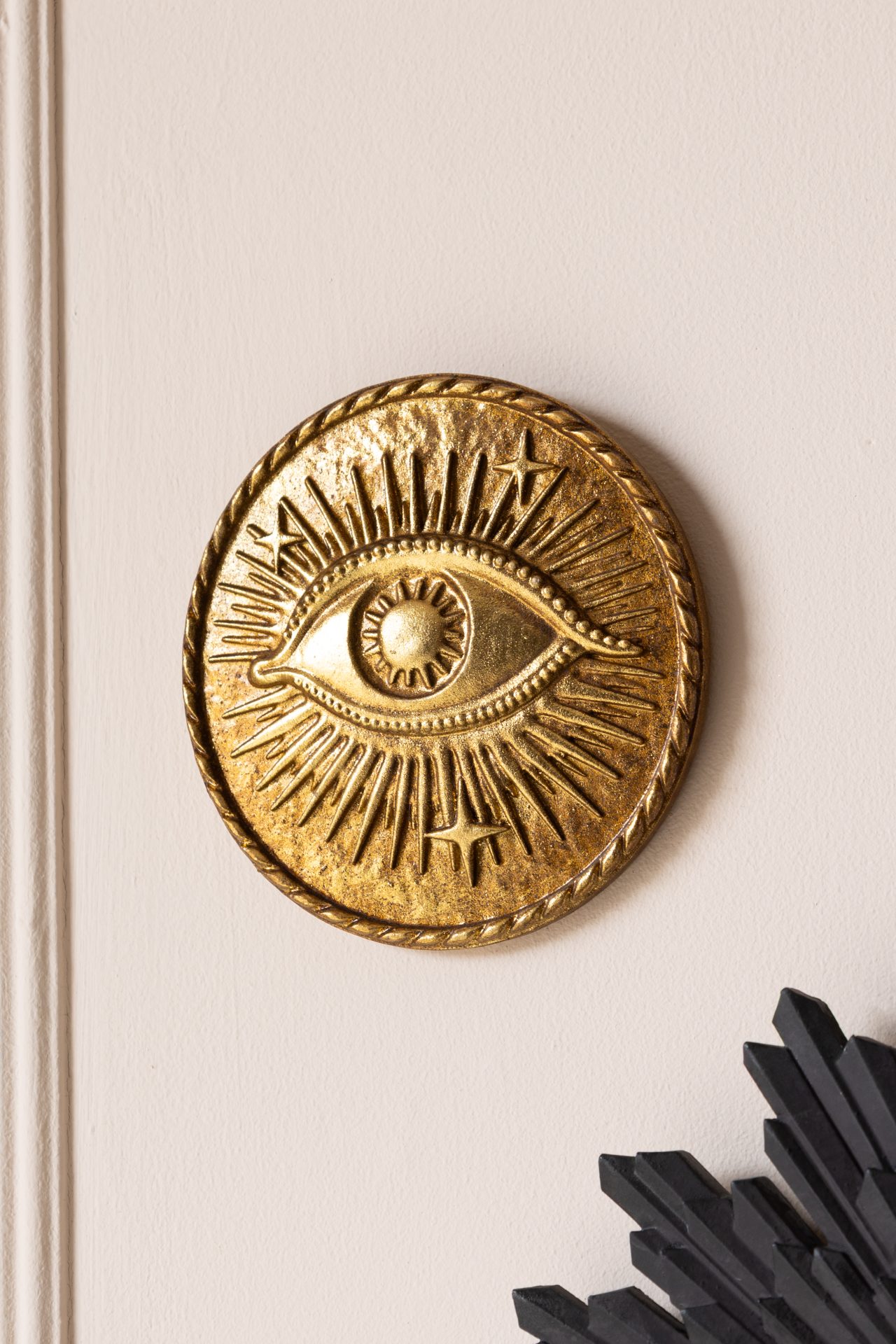 Circular gold medallion with eye design hung on a white wall