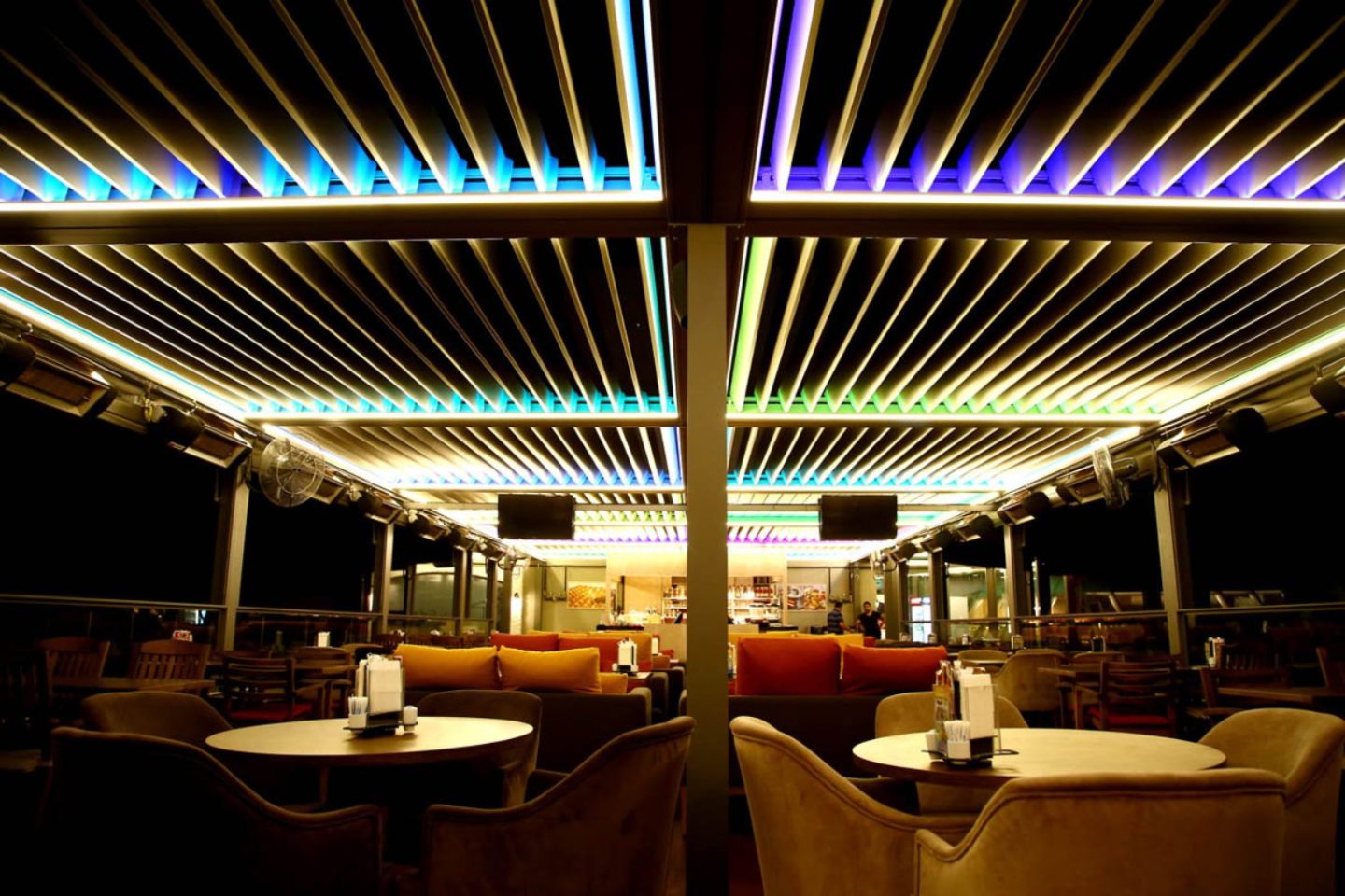 Metal pergola with coloured lights above cafe table and chairs at night