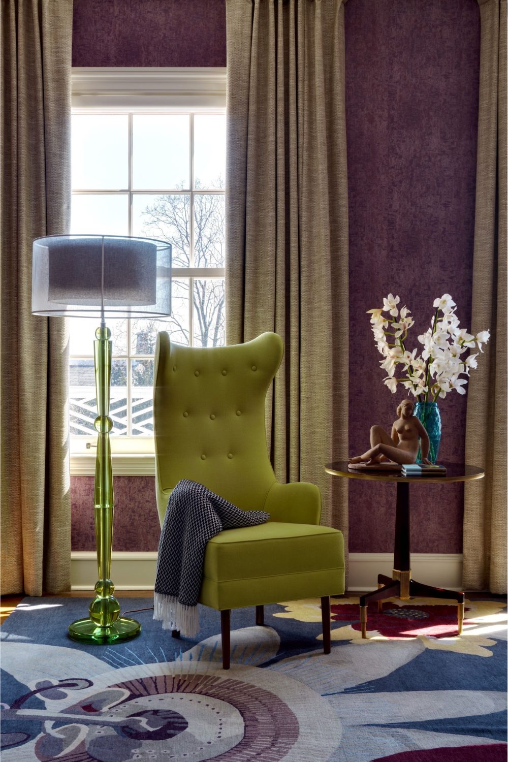 Green armchair and green standing lamp on blue rug in front of window covered with beige curtain