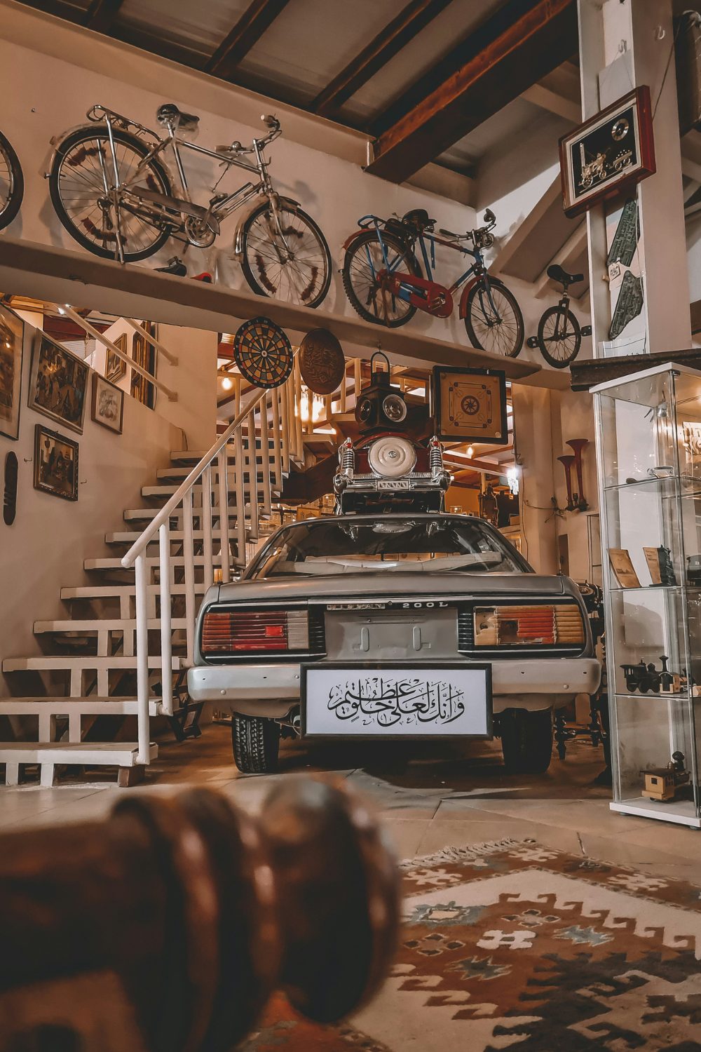Grey car parked next to white basement stairs with framed pictures, bikes and memorabilia on walls