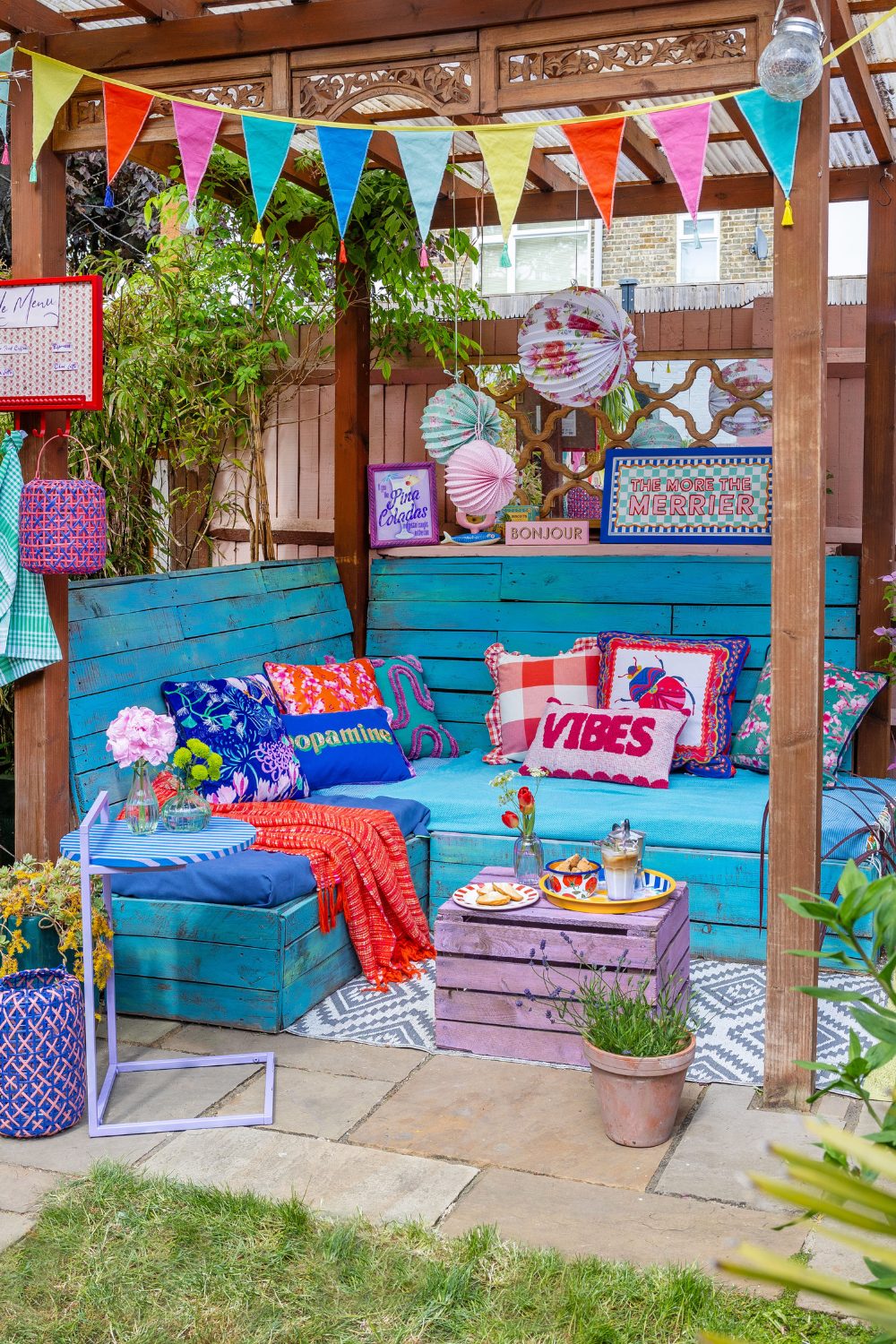 Wooden pergola with blue wooden seat, colourful cushions, bunting and paper lanterns