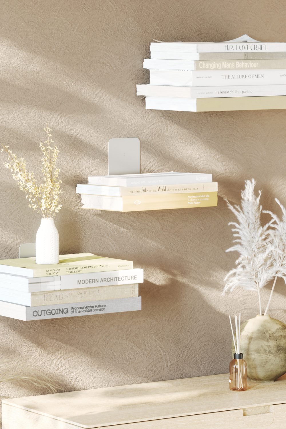 Three floating shelves holding white books on a white wall