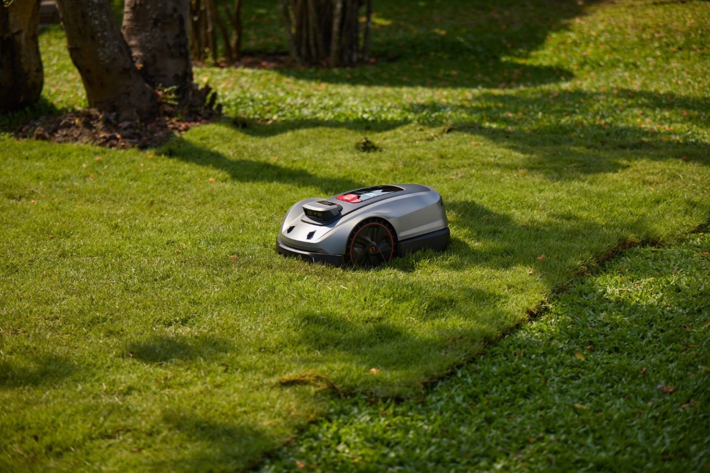Remote lawnmower on green lawn with trees