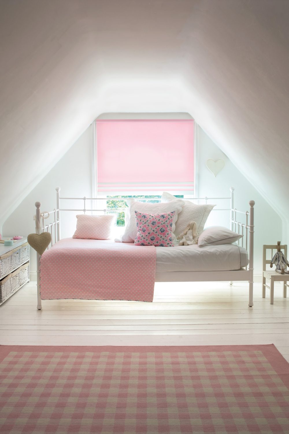 White bedroom loft conversion with white wooden floor, white daybed with pink cushions, pink blinds and pink gingham rug