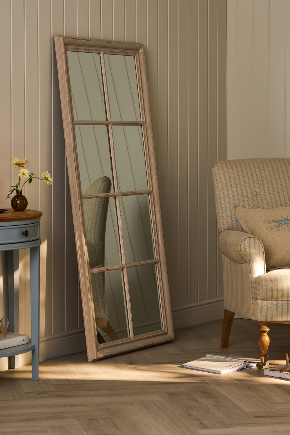 White wood panelled living room with large mirror leaning against wall on wooden floor next to white striped armchair