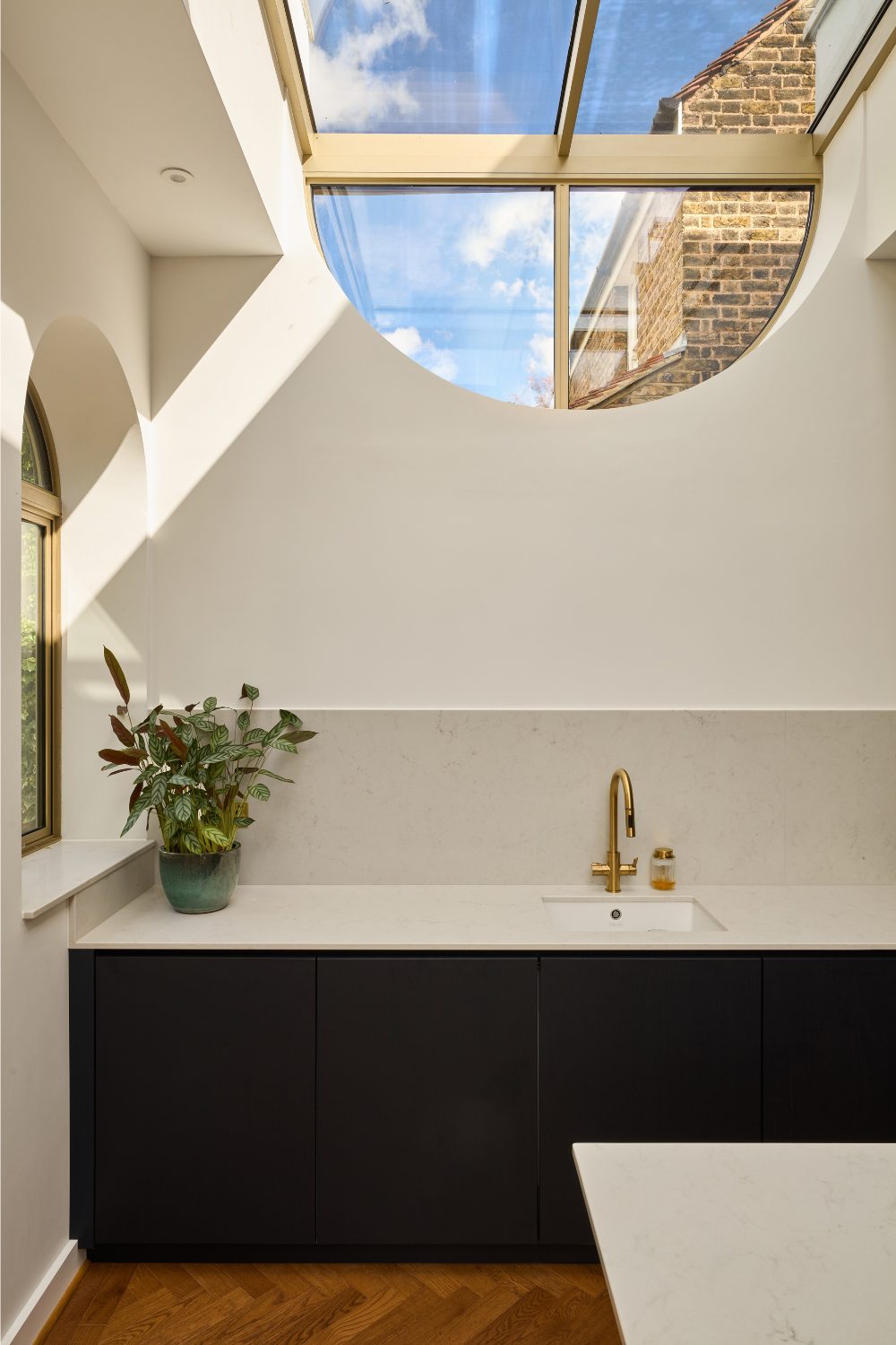 Kitchen with white marble worktops below a semi-circular skylight with view of blue sky