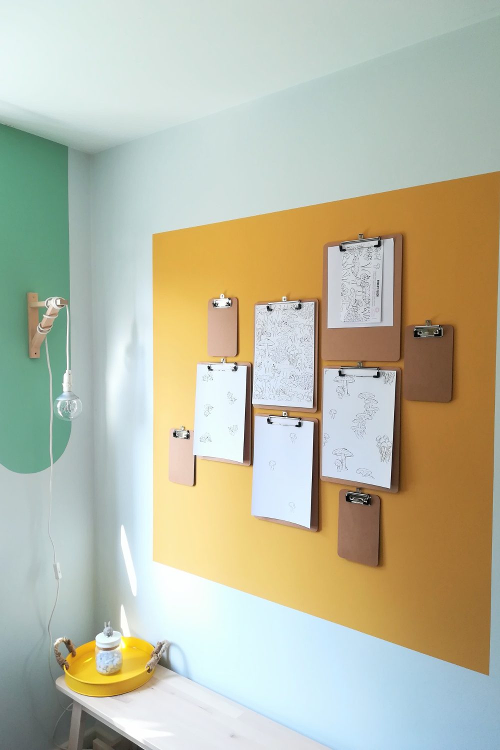 White wall with painted yellow and green areas hung with lamp and clipboards.