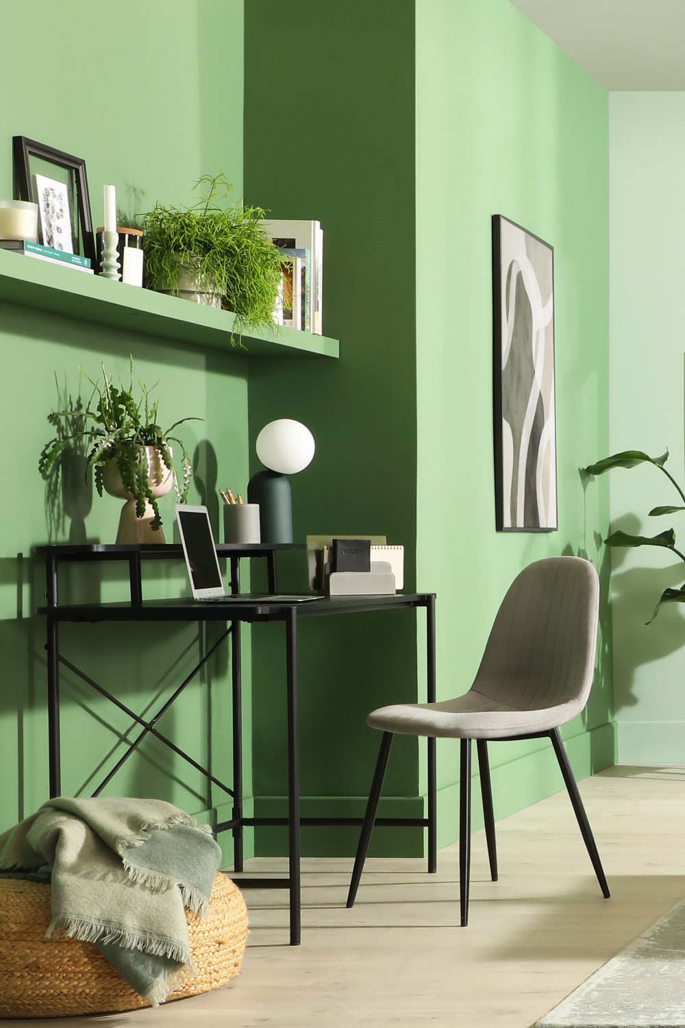 Green home office with black desk, grey chair and built in shelves holding books, pot plant and candle