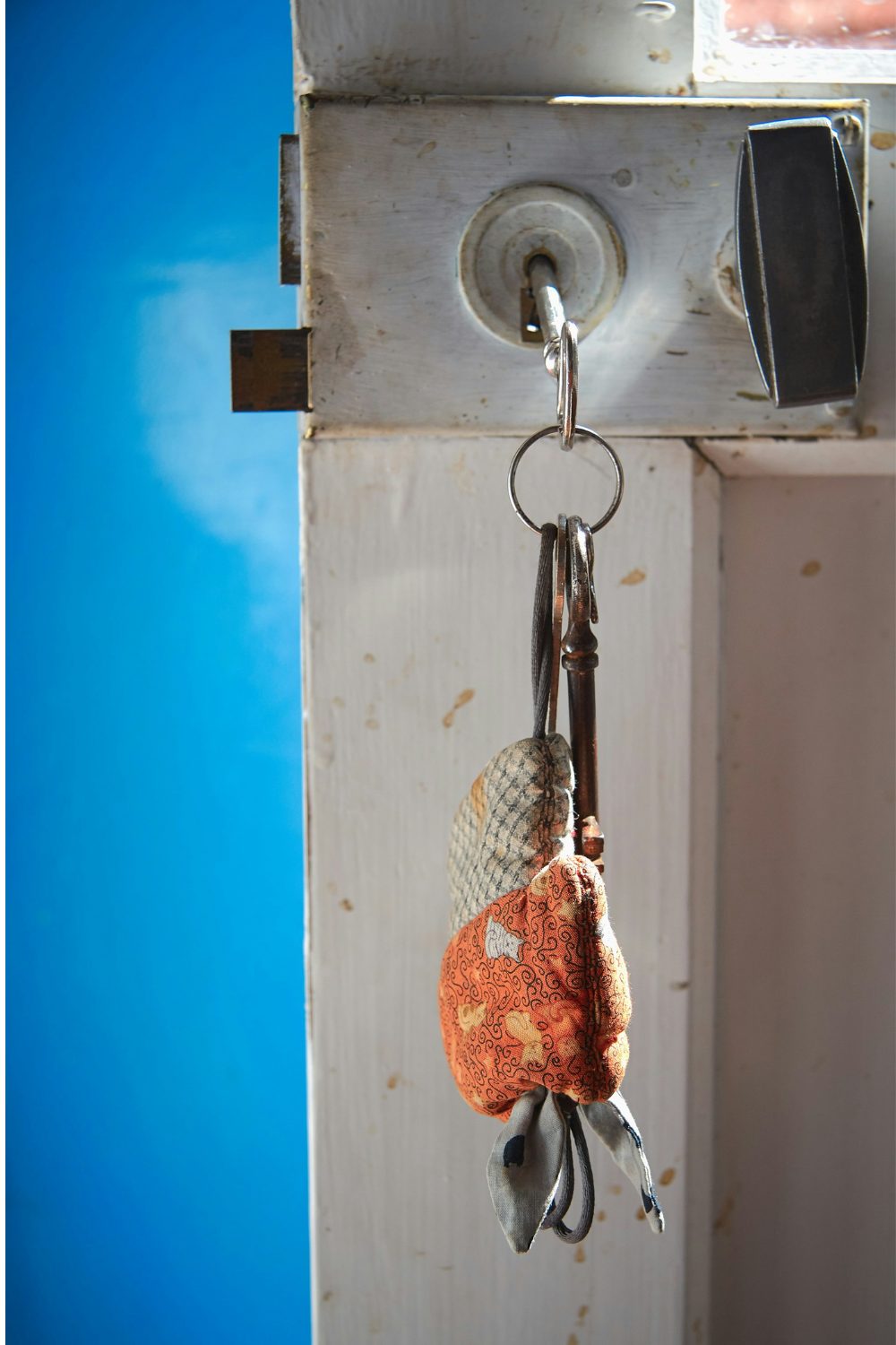 Silver key with orange cloth keyring in a white wooden door lock against blue sky background