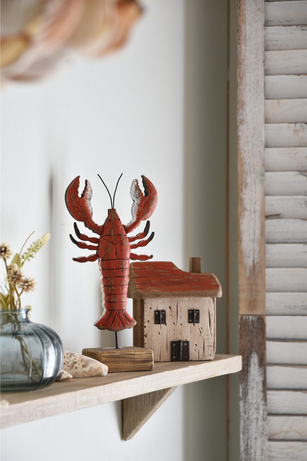 Wooden lobster and house models on wooden shelf next to distressed wood shutters 
