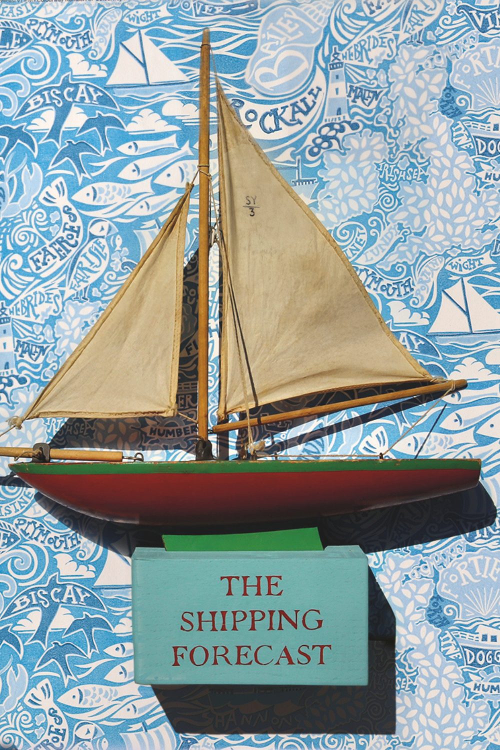 Wooden ship model and wood 'Shipping Forecast' block on blue sea patterned wallpaper