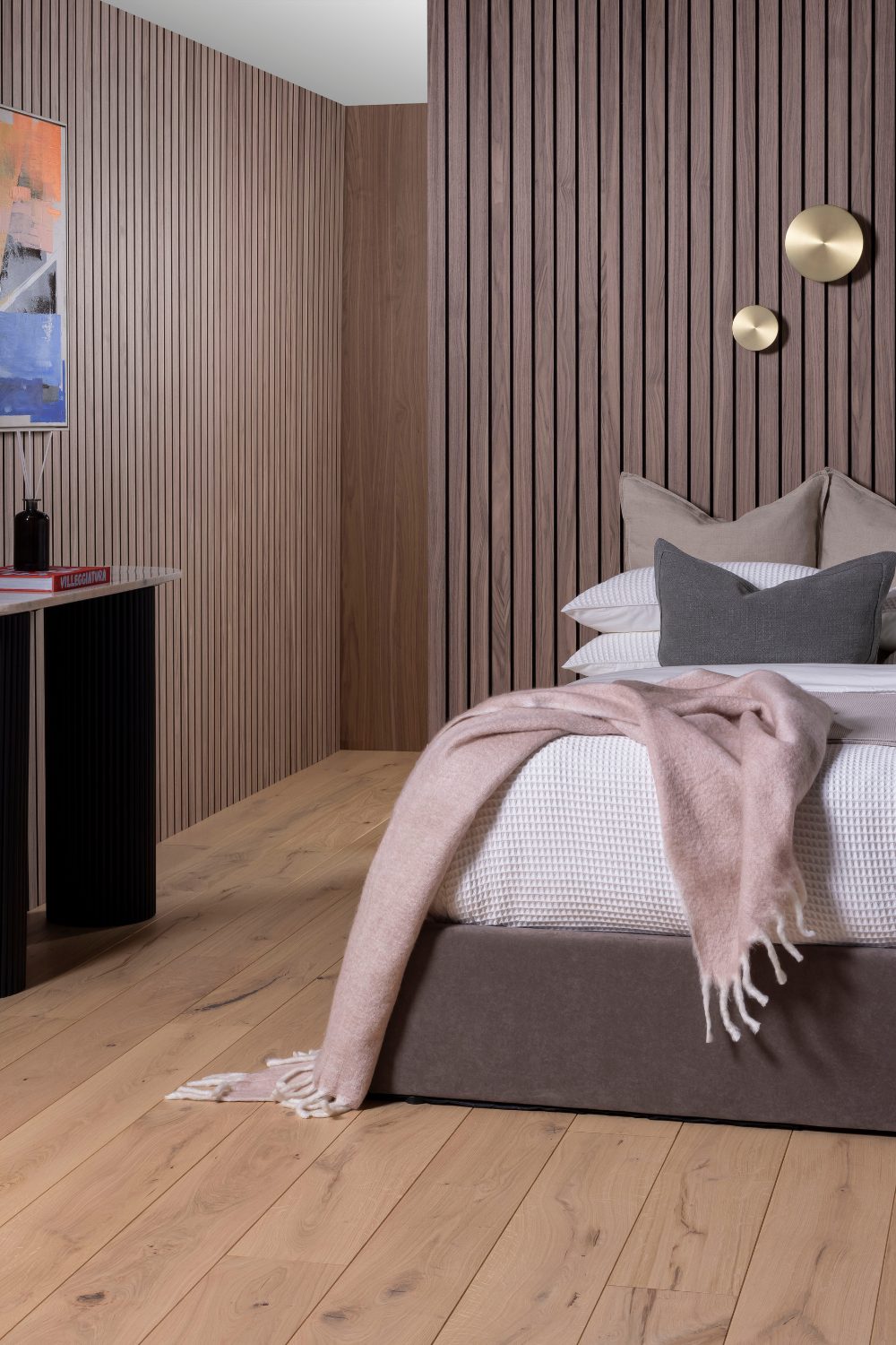 Bed with pink throw and black cabinet against wooden slatted walls and wooden floor