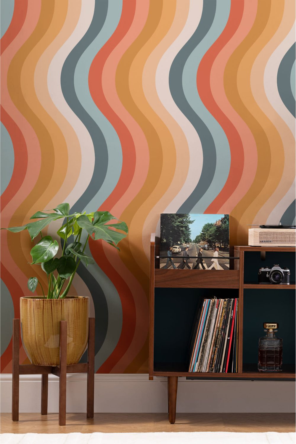 Wooden cabinet holding records and wooden plant pot against a multi-colour striped wall