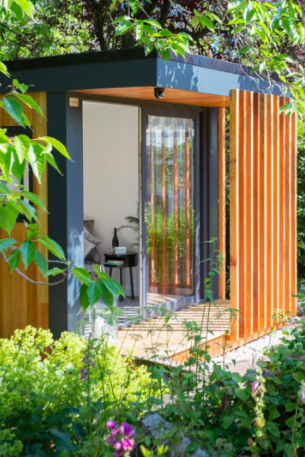 Garden room with glass door and wooden slatted screen with variety of plants