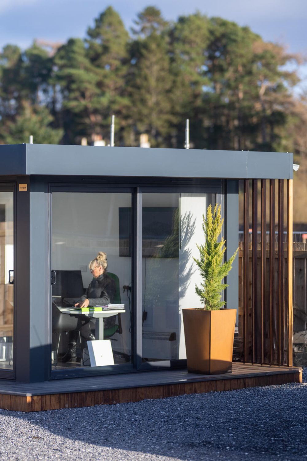 Woman at desk in garden room ofice with glass doors on a grey gravel surface